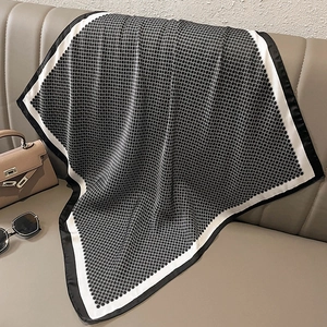 Close-up of black and white geometric silk scarf draped on a leather sofa with chic accessories
