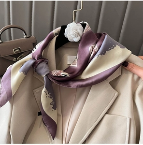 Close-up of silk scarf with purple and grey abstract patterns styled on a beige blazer