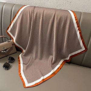 Brown geometric pattern silk scarf draped on a grey sofa with an orange border accent