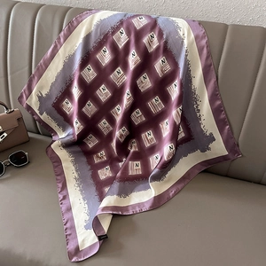 Close-up of silk square scarf with vintage letter N patterns draped on a leather sofa