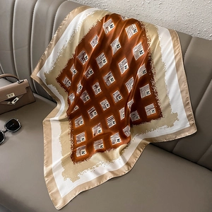 Close-up of geometric letter pattern on silk-feel scarf draped on a leather sofa