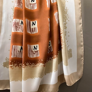 Detailed close-up of silk square scarf showing geometric pattern and letter N print texture