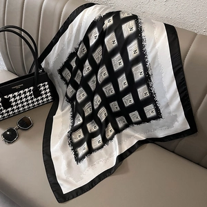Detailed view of square silk scarf with black white grid pattern on a leather sofa