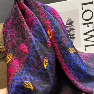 Elegant silk scarf with paisley and leopard print draped over a stylish leather handbag