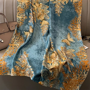 Luxurious dark blue silk scarf with golden butterfly and coral prints on a leather sofa