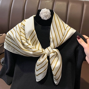 Elegant striped satin scarf in cream and gold worn over a black turtleneck sweater