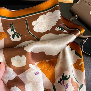 Écharpe élégante en soie avec motifs floraux orange présentée avec un sac en cuir