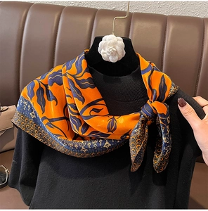 Dettaglio di un foulard in seta arancione con foglie blu su un maglione nero elegante
