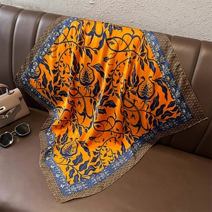 Dettaglio di un foulard in seta arancio e blu su divano in pelle con accessori eleganti