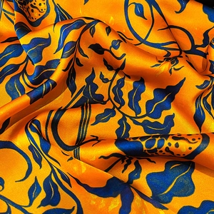 Dettaglio macro del tessuto foulard in seta con trama lucida e motivo floreale arancio blu