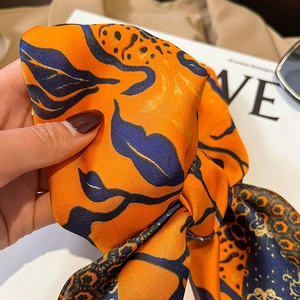Dettaglio di sciarpa in seta con stampa a foglie astratte arancioni e blu e leopardo