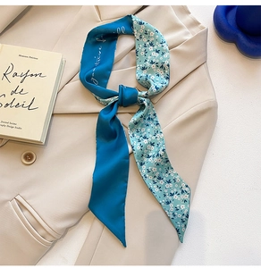 Détail d'un foulard étroit en soie bleue avec imprimé floral noué sur un blazer