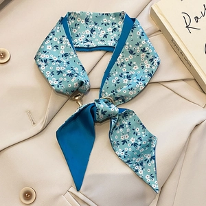 Détail d'un foulard en satin bleu à fleurs avec anneau doré sur un blazer crème