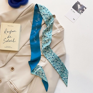 Détail d'une écharpe en soie bleue étroite avec motif floral et lettrage sur un blazer beige