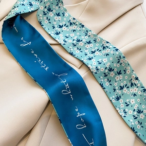 Détail d'un foulard twilly double face avec motifs floraux et écriture sur un blazer