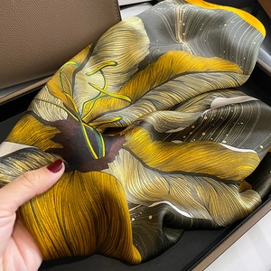 Detail of silk square scarf featuring yellow and grey floral prints on a leather gift box