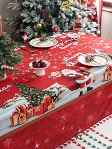 Detail of red Christmas tablecloth featuring Santa and tree patterns in festive setting