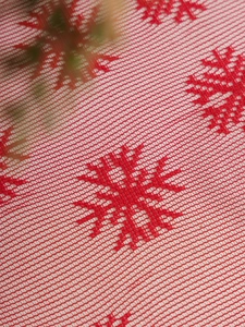Close-up of red Christmas tablecloth with white embroidered snowflakes and mesh texture