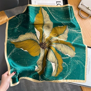Elegant emerald silk scarf with floral print and gold trim on white handbag background
