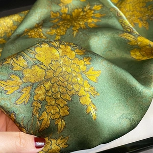 Detail of elegant dark green silk scarf with vibrant yellow flower pattern and satin texture