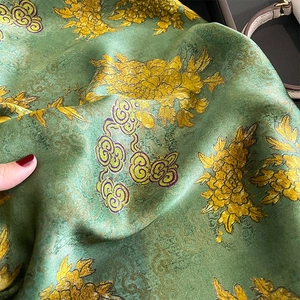 Detailed close-up of green silk scarf with gold chrysanthemum patterns and cloud prints