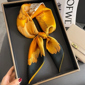 Detail of silk square scarf with yellow floral print tied in a bow on a black display tray