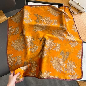 Elegant silk scarf featuring vibrant orange and gold floral patterns draped over furniture