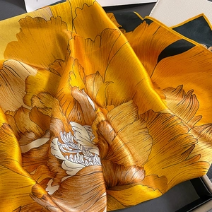 Close-up of silk square scarf featuring orange floral patterns and satin glossy finish