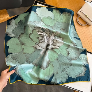 Detailed view of large floral print silk scarf with vibrant yellow hem on a wooden surface