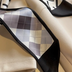 Détail du foulard twilly en soie gris avec motif losanges et texture lisse aux bords noirs