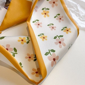 Detailed macro view of floral silk scarf with orange borders and twill weave texture