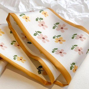 Close-up of floral twilly silk scarf with yellow satin edges on a textured background