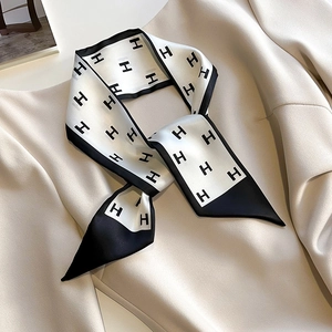 Élégant foulard étroit noir et blanc avec motif H noué sur le revers d'un tailleur beige
