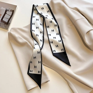 Détail d'un foulard twilly en soie à motif H noir et blanc sur un haut en maille beige