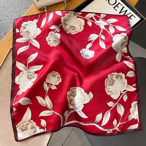 Detail of red silk square scarf with white floral roses displayed with a handbag