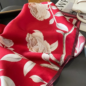 Detail of red silk scarf with white roses on grey table with beige handbag
