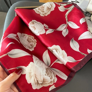 Detailed close-up of vibrant red silk scarf with white rose patterns and dark red borders