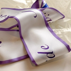 Dettaglio di un foulard in raso bianco con bordino viola e scritte corsive eleganti