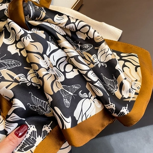 Close-up of silk scarf showing elegant butterfly floral patterns and gold satin edges