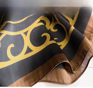 Detail view of the fine stitching and golden scroll pattern on a silk-like fashion scarf