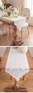 Detail eines weißen Vintage-Spitzentischläufers mit Blumenstickerei und Quasten
