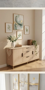 Detail of light wood sideboard with black handles, gold metal frame and plant wall art