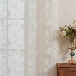 Détail de broderies florales blanches et bords festonnés sur rideaux en dentelle voilage