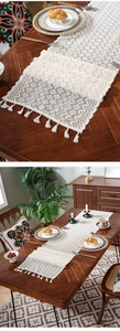 Detailed knit texture and tassels of a white crochet table runner on a wooden table