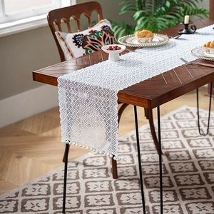Macro shot of white lace table runner with geometric mesh patterns and pompom tassels