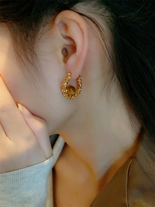Gros plan de la boucle d'oreille dorée en C avec texture argentée et perle oeil de tigre ambre