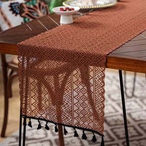 Detail of hollow lace table runner with geometric patterns and black fringe tassels
