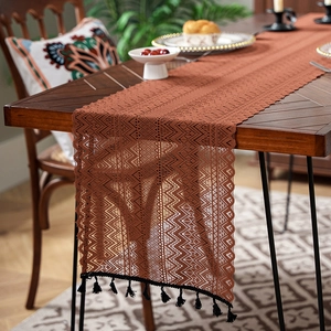 Detail of caramel knit table runner with geometric openwork and black tassels on wood