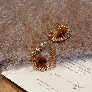 Boucles d'oreilles créoles avec œil de tigre et texture dorée sur fond en peluche