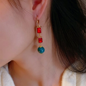 Detail of vintage gold earrings with red crystal glass and blue bead on model